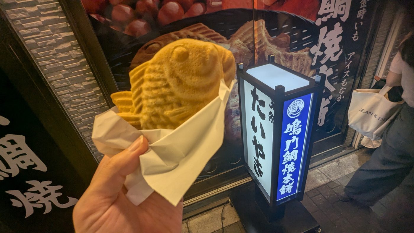 A fish-shaped taiyaki pastry held in front of the shop